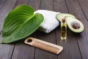 White towel, avocado, little glass bottle and wooden comb for hair lie on a wooden table