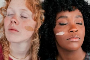 Close-up of an african and caucasian woman's face with skin tone foundation cream on cheek