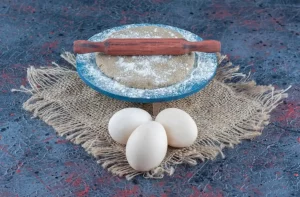 Three uncooked fresh chicken eggs with dough on a sackcloth.